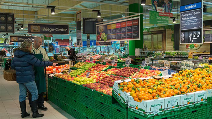 Chez Real, des clients regardent des fruits mis en lumière par l'éclairage de supermarchés Philips