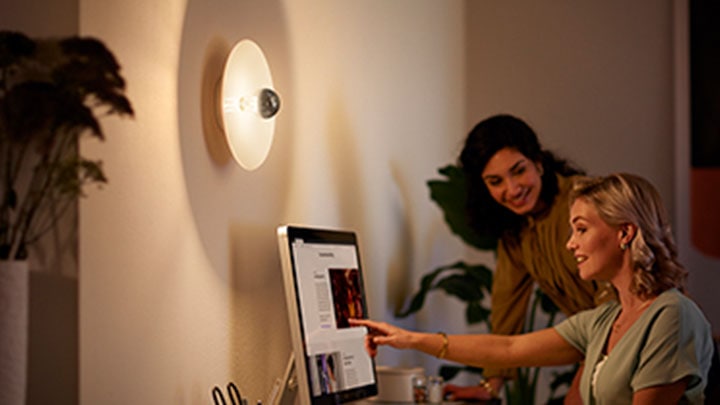 Femmes travaillant à l'ordinateur à côté d'une ampoule de miroir LED murale Philips