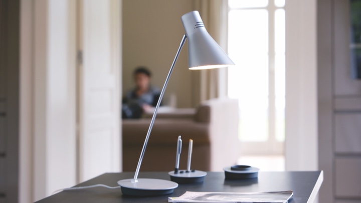 Une lampe à poser sur un bureau, dirigée sur du papier et des stylos