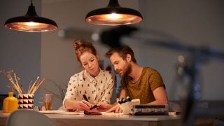 "Des suspensions LED élégantes projettent une lueur chaleureuse sur un couple travaillant ensemble, mettant en valeur un éclairage économe en énergie pour des tâches productives en soirée. »