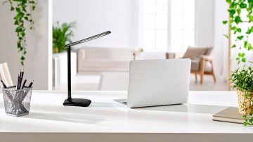 Dans une pièce d'un blanc éclatant, on aperçoit une lampe à poser et un ordinateur portable sur un bureau.