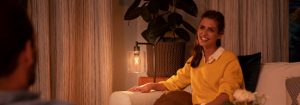 "Ambiance de salon cosy créée par une lampe de table LED chaleureuse, éclairant une femme en pull jaune profitant d'une conversation en soirée. »