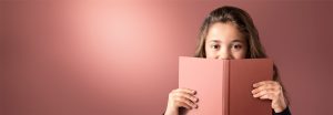 "Une jeune fille regarde par-dessus un livre rose sur un fond éclairé par une lumière LED douce, présentant un éclairage chaleureux et uniforme pour des environnements de lecture confortables."